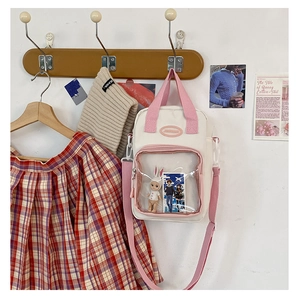 Close-up of a white canvas ita bag with a clear PVC window and pink handles hanging on a hook