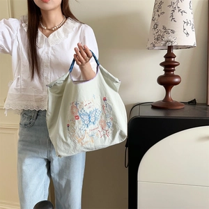 Détail de broderie papillon bleu et motifs floraux sur un sac cabas en oxford vert clair