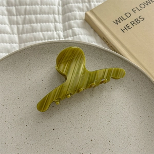 Detail view of a green ombre acetate claw clip on a decorative plate and white quilt background