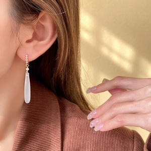 Detailed view of teardrop earrings with gold metal bars and small pearl accents