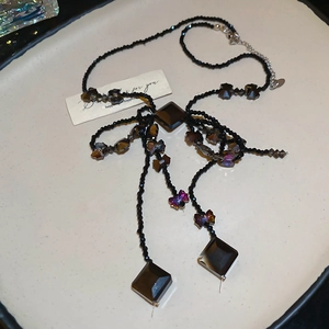Macro detail of black beaded necklace with gradient purple butterfly and faceted gem pendant