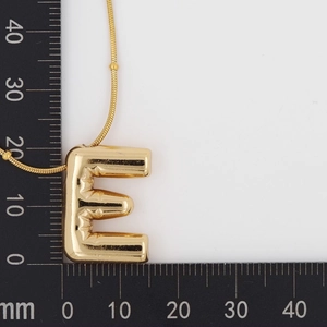 Macro view of a 3D puffy gold letter E pendant measured at 28mm on a ruler