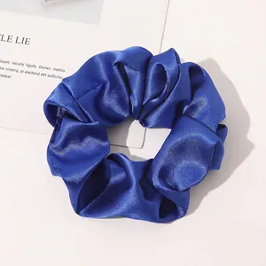 Close-up of royal blue silk satin scrunchie with smooth texture on white background