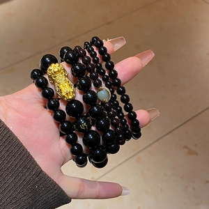 Detail of stacked obsidian bead bracelets with golden Pi Xiu and mantra symbols