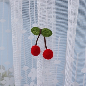 Close-up of decorative red cherry plush accessory on a white lace curtain panel