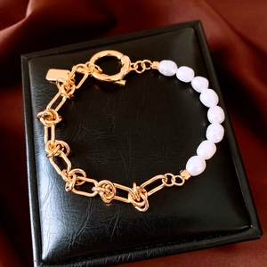 Macro detail of 18k gold-plated chain and white pearls on a black leather jewelry box