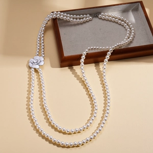 Elegant layered pearl necklace with a white camellia flower pendant on a wooden tray