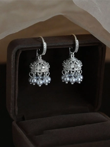 Detailed close-up of hollow bell earrings with shiny zircons and pearl tassels on velvet