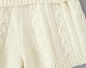Détail macro du tricot torsadé blanc cassé et de la taille côtelée du short en maille