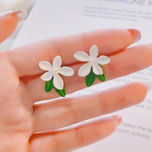 Detailed view of handmade flower stud earrings with white petals and green leaves on hand
