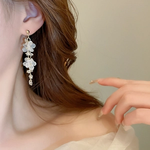 Detail of floral tassel earrings with white resin petals and gold finish on model