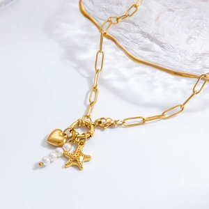 Close-up of gold paperclip chain necklace with heart, starfish and white pearl charms