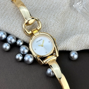 Detail view of gold horseshoe-shaped watch with white dial on elegant pearl background