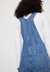 Detail of Y-back denim overalls featuring rear pockets and classic contrast stitching
