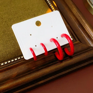 Detail of minimalist red C-shaped hoop earrings displayed on a vintage wood frame
