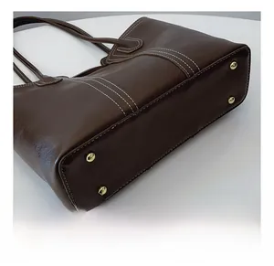 Detailed view of dark brown tote bag base featuring four golden protective metal studs