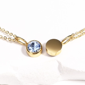 Detailed view of gold necklace with blue gemstone and polished disc on white stone