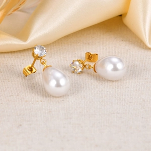 Detailed shot of golden pearl earrings with clear zircon stones on a silk fabric background