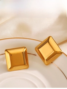 Detailed view of square gold stud earrings with polished finish on a porcelain dish