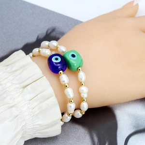 Freshwater pearl bracelet with blue and green evil eye charms on a woman's wrist