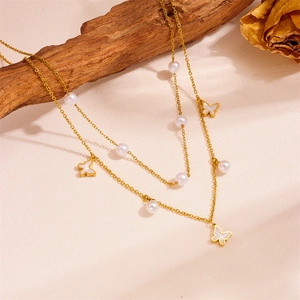 Détail d'un collier doré double rang avec perles et breloques papillons sur bois
