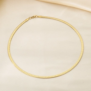 Macro detail of 6mm golden flat herringbone chain necklace on beige silk background