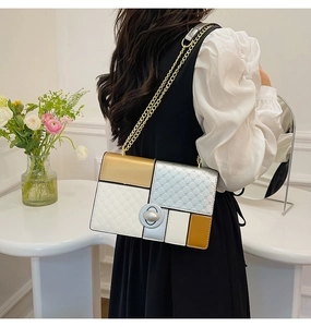 Detail of color-block shoulder bag with quilted texture and gold chain strap worn by model