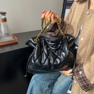Black quilted bucket bag with gold chain strap and drawstring closure in lifestyle setting
