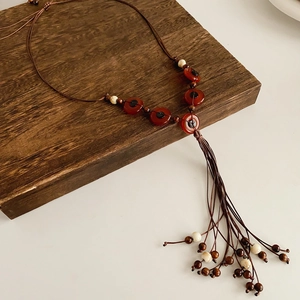 Detail of bohemian necklace with red resin rings and woven cord on dark wood