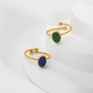 Detail of 18K gold-plated rings set with oval blue and green stones on a white stand