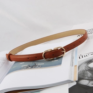 Detail of slim brown leather belt with gold horsebit buckle on magazine background