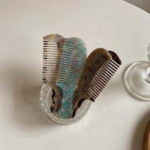 Portable acetate hair combs in amber and blue shell patterns in a glass cup