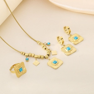 Dettaglio del set di gioielli in oro martellato con pietre turchesi quadrate su tessuto beige