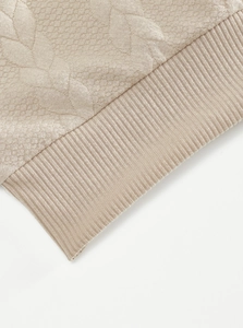 Detailed close-up of beige jacquard knit texture and dense ribbed hem craftsmanship
