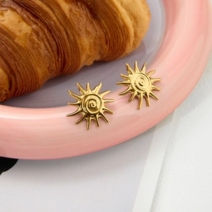 Gros plan de boucles d'oreilles soleil dorées sur plateau en céramique rose élégant