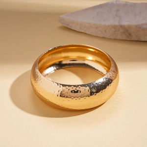Close-up of golden wide cuff bracelet featuring handcrafted hammered texture and metallic shine