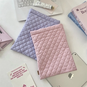 Detail of diamond-quilted soft laptop sleeves in lavender and pink colors on a white desk