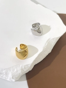 Detailed top view of 18K gold and silver U-shaped ear cuffs on textured rock and leather