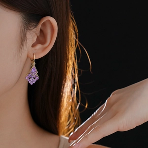 Detail of elegant gold hoop earring with purple diamond-shaped leaf pendant on a model