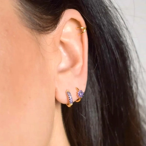 Detailed close-up of floral gold earrings with purple zircon stones on a model's ear