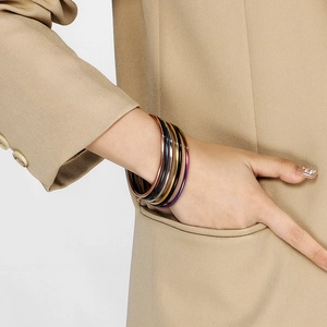 Polished titanium steel layered bangles in multiple colors worn with a beige suit