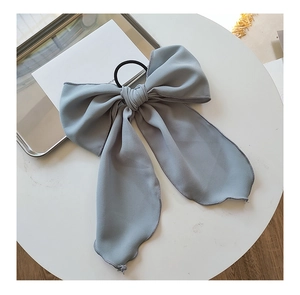 Close-up of a large grey fabric bow hair tie with elegant draping on a white surface