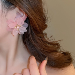 Detail of pink matte flower earring with pearl stamen worn by model on beige background