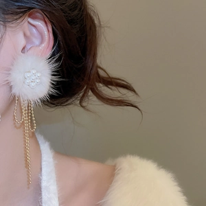 Detail of flower stud earrings with white pom-pom and long gold chain fringe on model