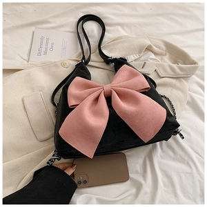 Detail of black leather bag with a pink oversized bow and chain strap next to a phone