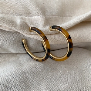 Chic C-shaped tortoiseshell resin earrings with gold accents on a beige linen background