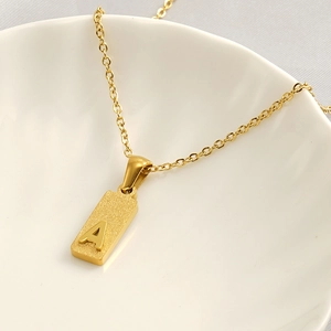 Macro view of gold plated square pendant with embossed letter A on a ceramic bowl