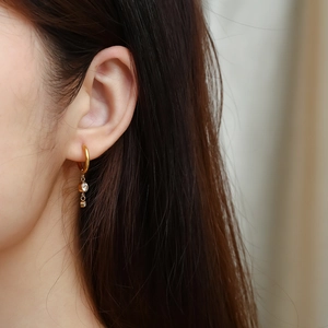 Close-up of gold hoop earrings with double zircon pendants on woman's ear
