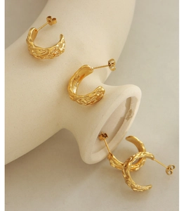 Detailed view of textured gold C-shape earrings displayed on white frosted ceramic plate