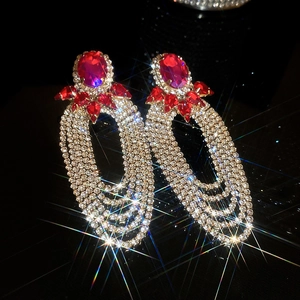 Close-up of long tassel earrings with oval red gems and sparkling crystal fringe